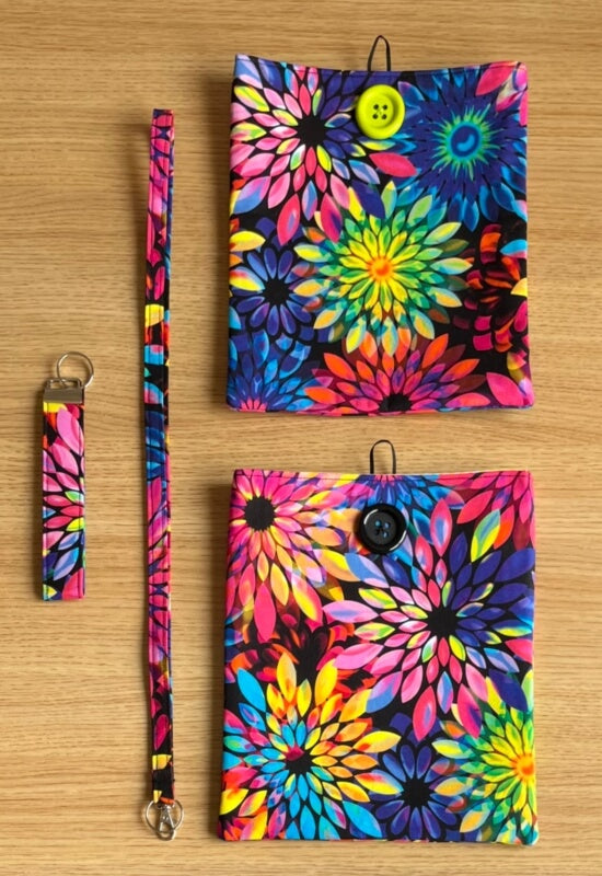 Kaleidoscope Dream handmade collection featuring book sleeves, a wristlet keychain, and a lanyard in a vibrant multicolor floral pattern on black fabric
