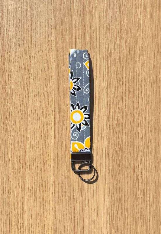 Citrus Garden wristlet keychain with bold yellow and white floral print on dark gray fabric